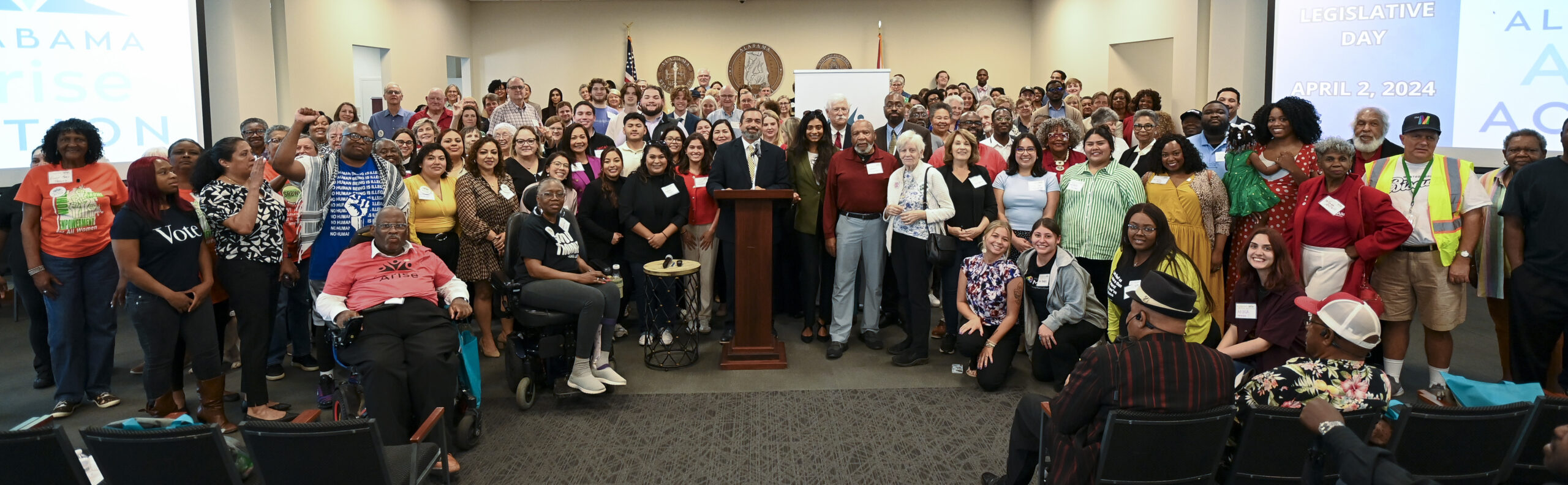 More than 100 people stand around a podium for a posed picture following a news conference.
