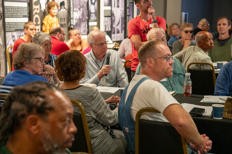 A person speaks at a table where others are listening.
