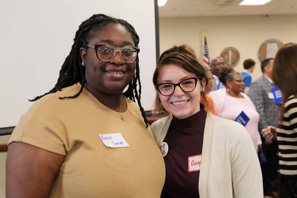 Two woman standing side-by-side smiling.