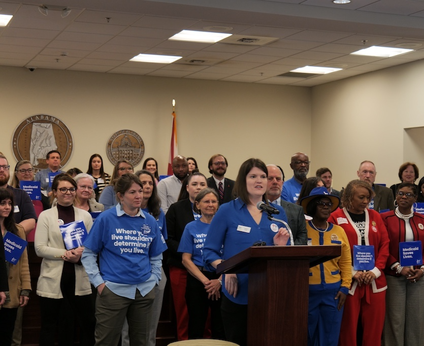 A woman speaks at a podium with several supporters standing beside her.