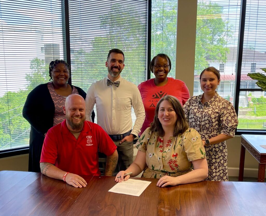 5 adults sitting at or standing by a table smiling after signing a contract.