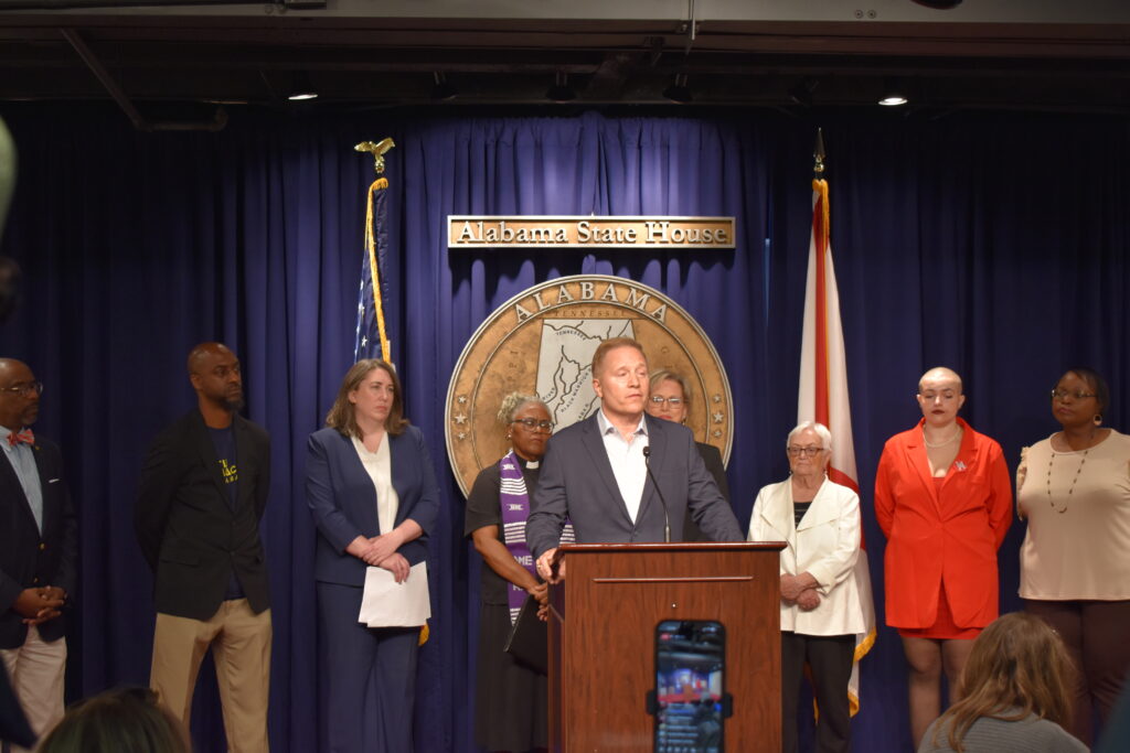 A man speaks behind a lectern with advocates standing behind him.
