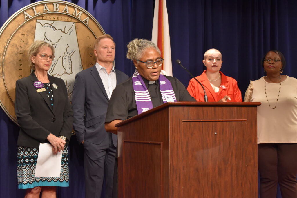 A woman speaks behind a lecture with advocates standing behind her.