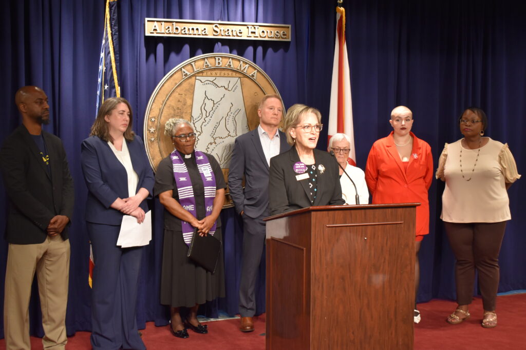 A woman speaks behind a lectern with advocates standing behind her.
