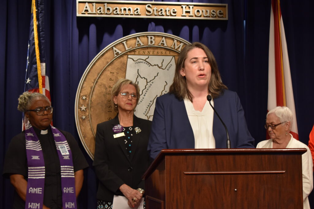 A woman stands behind a lectern with advocates standing behind her.
