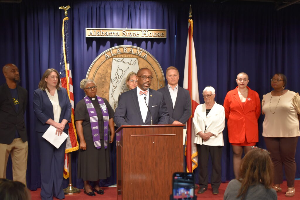 A man speaks behind a lectern with advocates standing behind him.