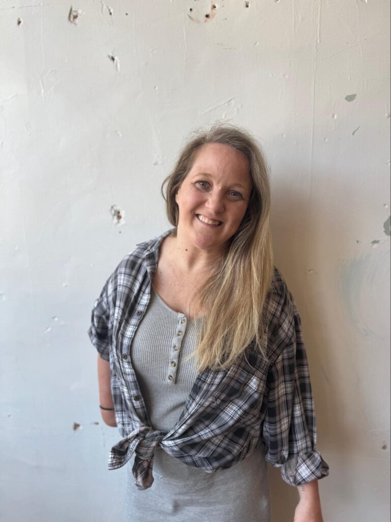 An adult woman stands in front of a wall. 