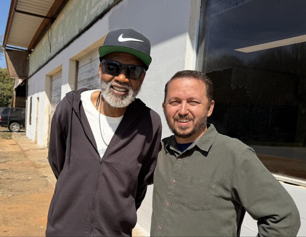Two men smile and embrace for a posed photo.