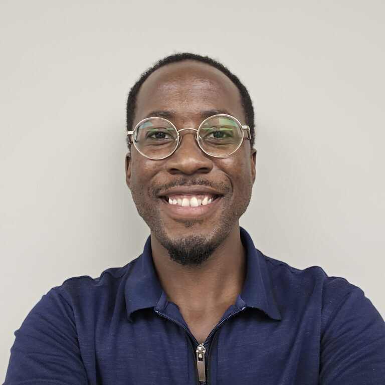 A smiling Black man wearing glasses and a dark blue shirt.